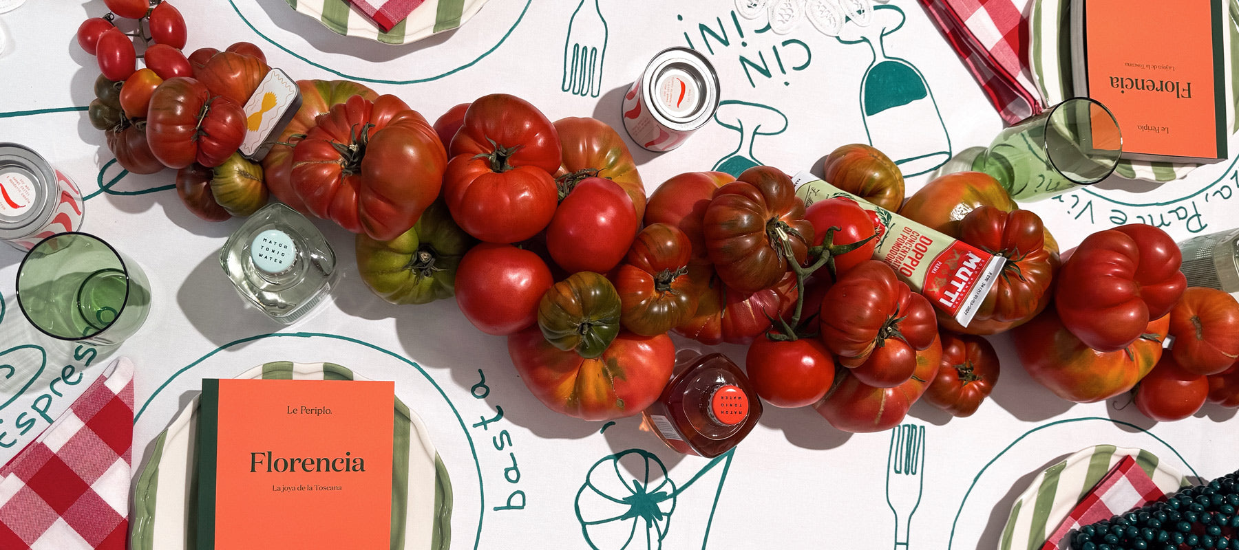 Mesa decorada con tomates y mantel ilustrado la temática de la guía de Florencia, con las guías impresas de Le Periplo y Match Tonic Water, tónicas de sabores.