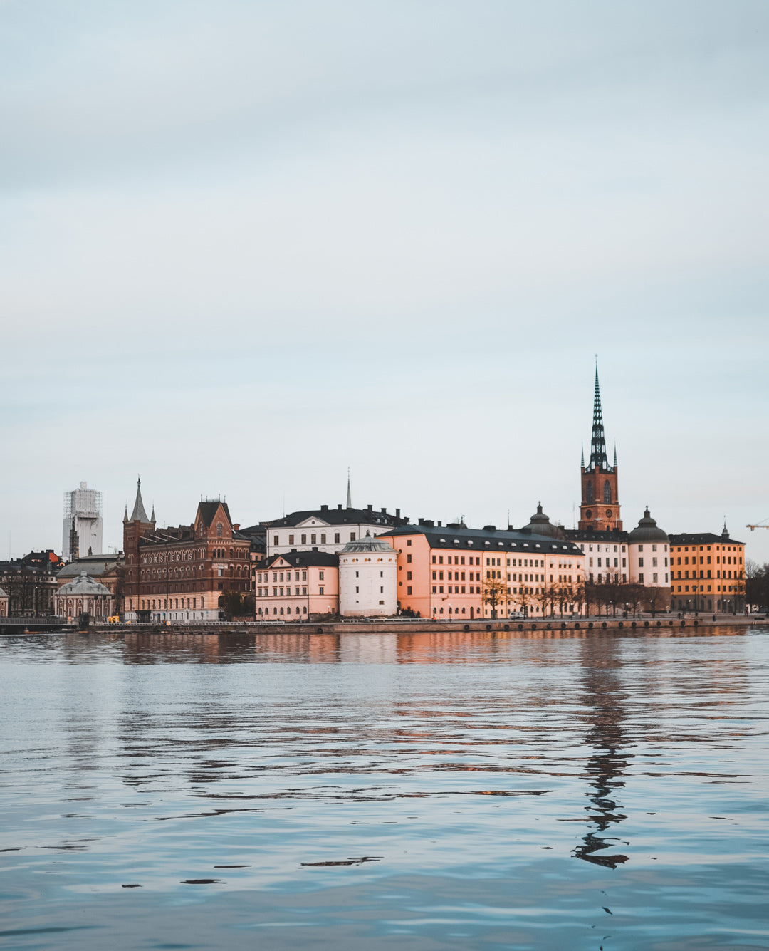 Vista panorámica de Estocolmo desde el agua, con edificios clásicos y la aguja de una iglesia reflejándose en el mar. Fotografía para la guía de viaje con recomendaciones y recorridos locales para descubrir la esencia auténtica de la ciudad sueca.