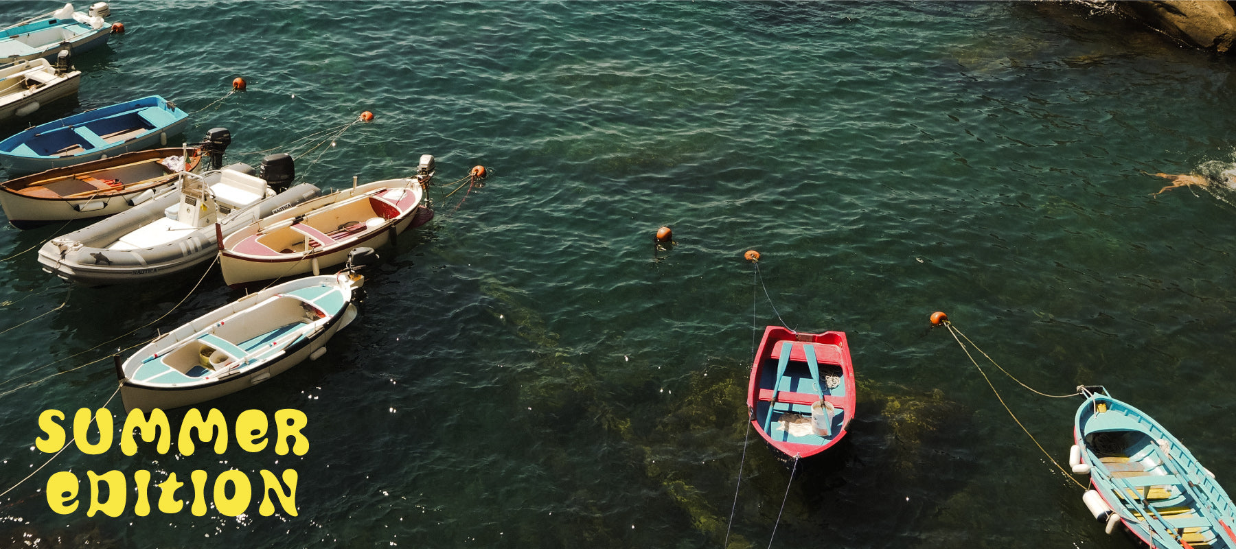 Vista de la costa italiana en verano, con aguas turquesas y pequeñas barcas de pescadores flotando cerca de un pintoresco pueblo costero. Obtén un 20% de descuento por la compra de una guía, descuento canjeable en el siguiente pedido.