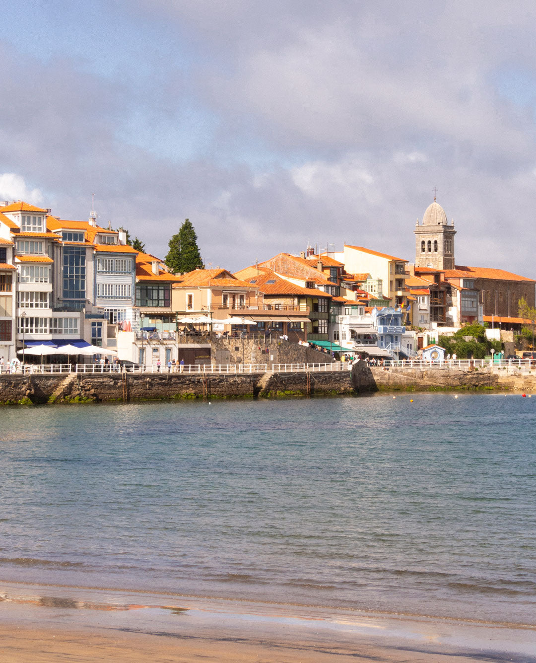 Pueblo pesquero asturiano con casas de colores junto al puerto, rodeado de verde y mar.