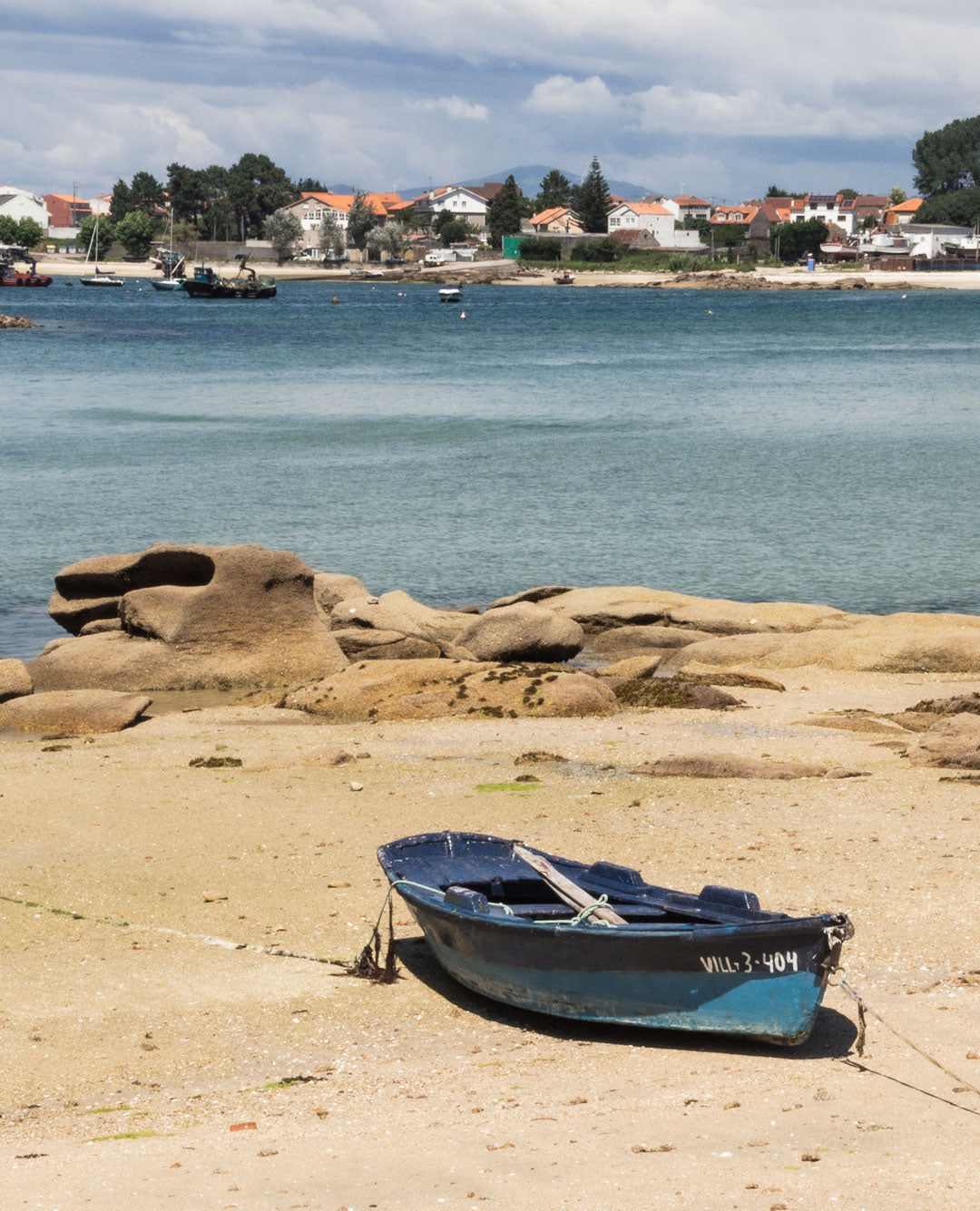 Vista de un puerto pesquero en Punta Moreiras en O Grove con barcos amarrados y redes marineras secándose al sol.